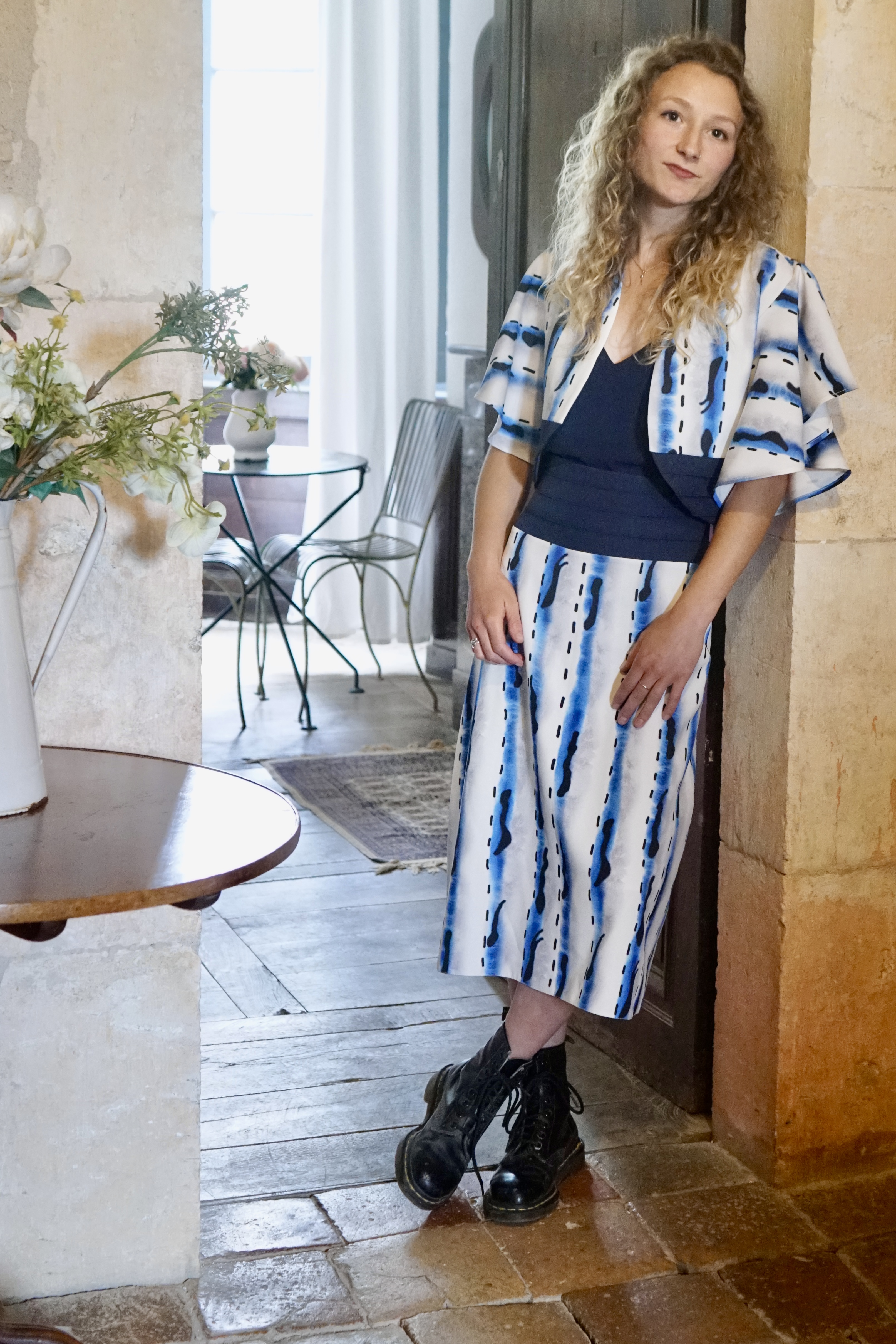 Leaning on the doorway a model in downward blue striped blue  dress and bolero